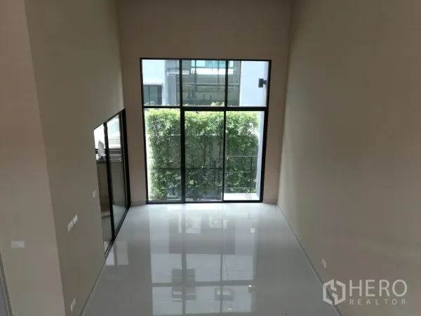 Townhouse for rent or sale in Suan Luang, Bangkok - Double-height living area with floor-to-ceiling windows and glossy tile floor.