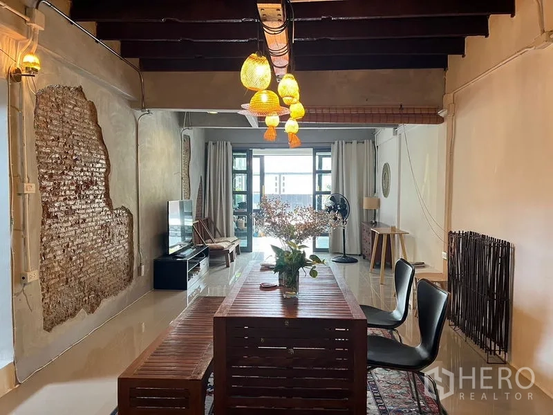 Townhouse for rent in Ratchathewi, Bangkok - Open-plan living and dining room with exposed brick, long wooden table and pendant lights.