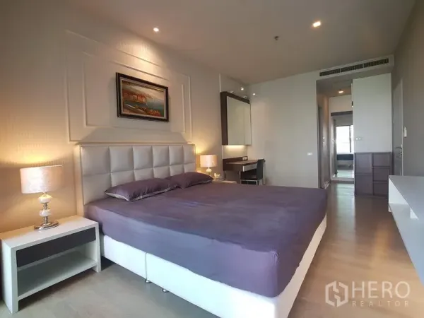 Condominium for rent in Bangkok - Spacious bedroom featuring a king bed, warm lighting, built-in vanity and storage near the corridor.