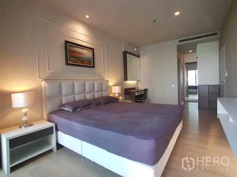 Condominium for rent in Bangkok - Spacious bedroom featuring a king bed, warm lighting, built-in vanity and storage near the corridor.