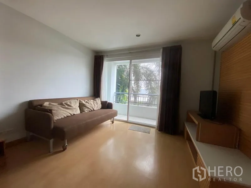 คอนโด ให้เช่าในWatthana, Bangkok - โซนพักผ่อนพร้อมโซฟาสีน้ำตาล ชั้นวางทีวี และประตูกระจกเปิดสู่ระเบียง