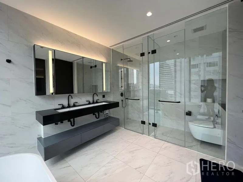 Condominium for rent in Bang Rak, Bangkok - Luxury bathroom with twin glass enclosures for shower and toilet.