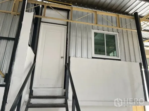 Warehouse for rent in Suan Luang, Bangkok - Mezzanine office with door and window accessed by black metal stairs inside the warehouse.