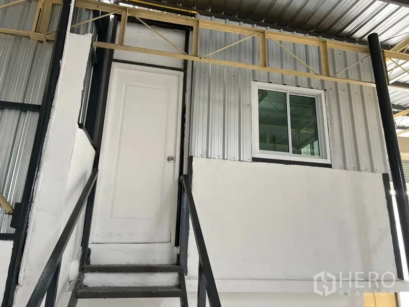 Warehouse for rent in Suan Luang, Bangkok - Mezzanine office with door and window accessed by black metal stairs inside the warehouse.