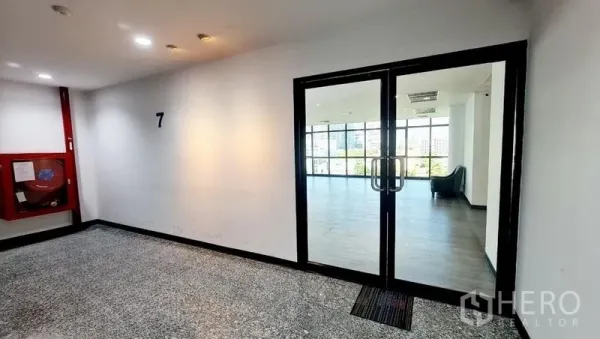 Office Space for rent in Watthana, Bangkok - Glass double doors opening to a bright office floor from the lift lobby with a fire hose cabinet on the wall.