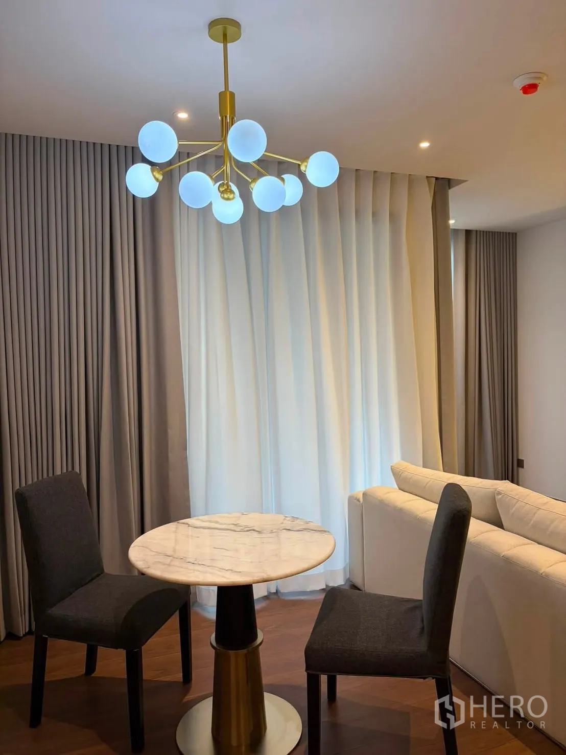Condominium for rent in Watthana, Bangkok - Dining nook with round marble table, two chairs, and a modern chandelier near the sofa.