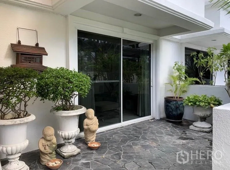 Townhouse for rent in Khlong Toei, Bangkok - Private stone‑tiled terrace with potted plants, garden statues and sliding glass entry.