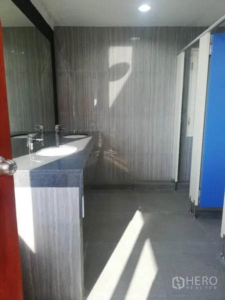 Office Space for rent in Watthana, Bangkok - Modern office restroom with double sinks, stone countertop, gray wall tiles, and partitioned stalls.