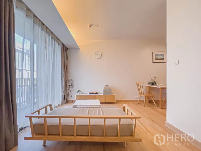 คอนโด ขายในWatthana, Bangkok - มุมนั่งเล่นมีเดย์เบด โต๊ะกลาง ตู้วางของเตี้ย และโต๊ะทำงาน ข้างผ้าม่านโปร่งเต็มความสูง