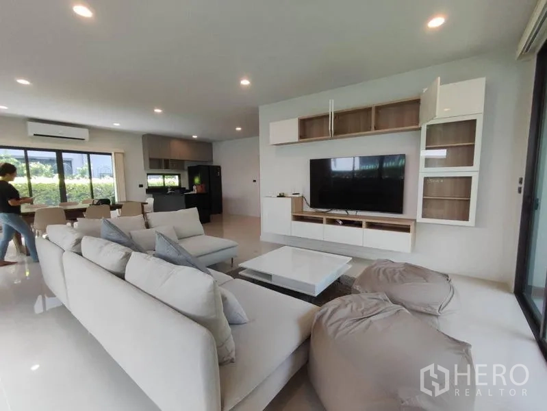 Detached House for rent in Bang Kapi, Bangkok - Open-plan living and dining area with sectional sofa, TV wall unit and kitchen beyond.