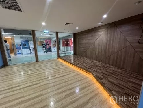 零售空间 出租在Bang Rak, Bangkok - 仿木地板与特色墙面搭配暖色LED灯带，临近玻璃店面。