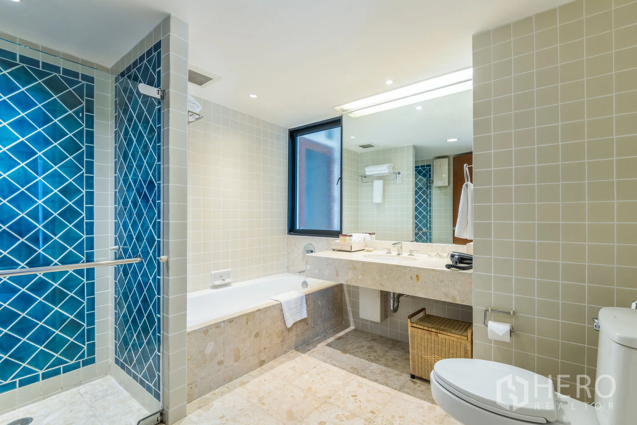 Condominium for rent in Yan Nawa, Bangkok - Bathroom with bathtub, separate glass shower lined with blue tiles and a large vanity.