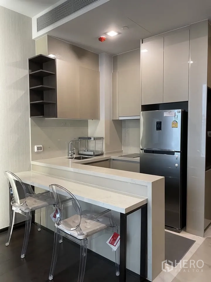Condominium for rent in Watthana, Bangkok - Compact modern kitchen with glossy cabinets, breakfast bar, and stainless refrigerator.
