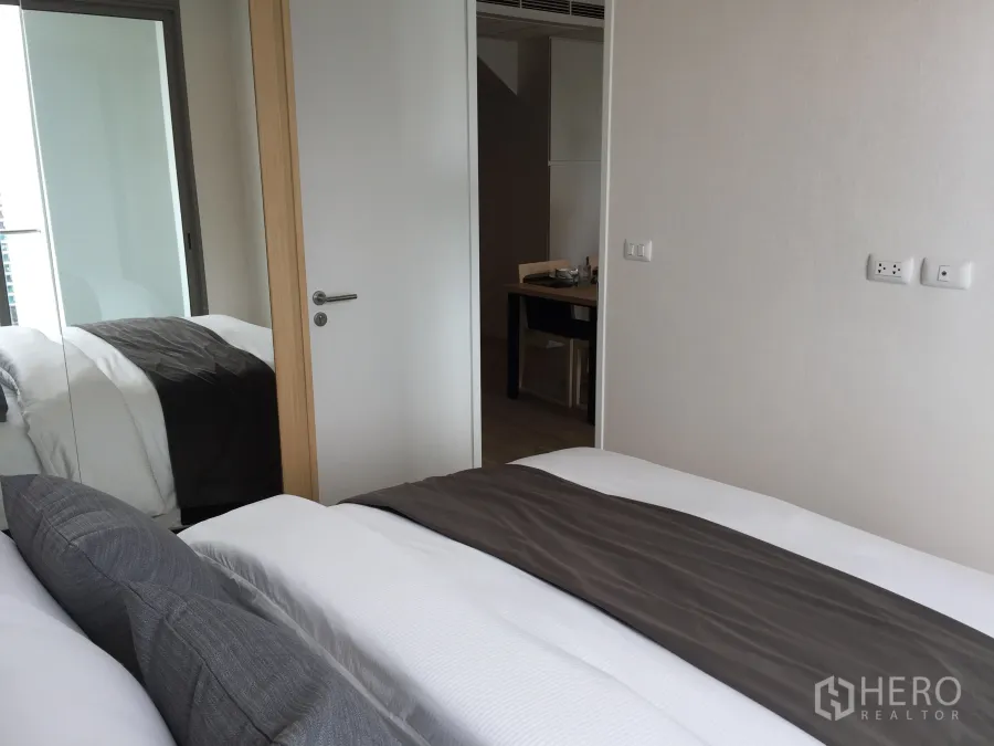 公寓 出售在Bang Rak, Bangkok - 卧室配镜面衣柜与灰色床品，邦拉区公寓内的滑动落地窗带来采光。