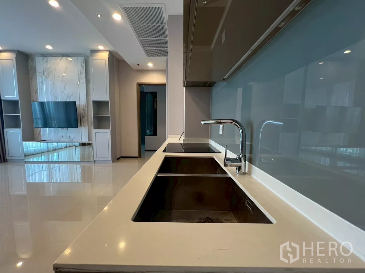 Condominium for rent in Phra Khanong, Bangkok - Kitchen countertop with dual sinks and glass splashback facing living room.