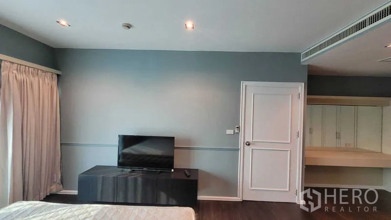 คอนโด ให้เช่าในKhlong Toei, Bangkok - ผนังห้องนอนใหญ่ วางทีวีบนตู้เตี้ย ประตูกระจกพร้อมผ้าม่าน และประตูภายในสีขาว