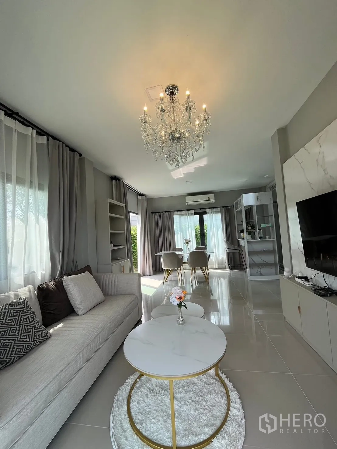 Detached House for rent in Bang Phli, Samut Prakan - Open-plan living and dining room with chandelier, sofa, TV wall and large windows.