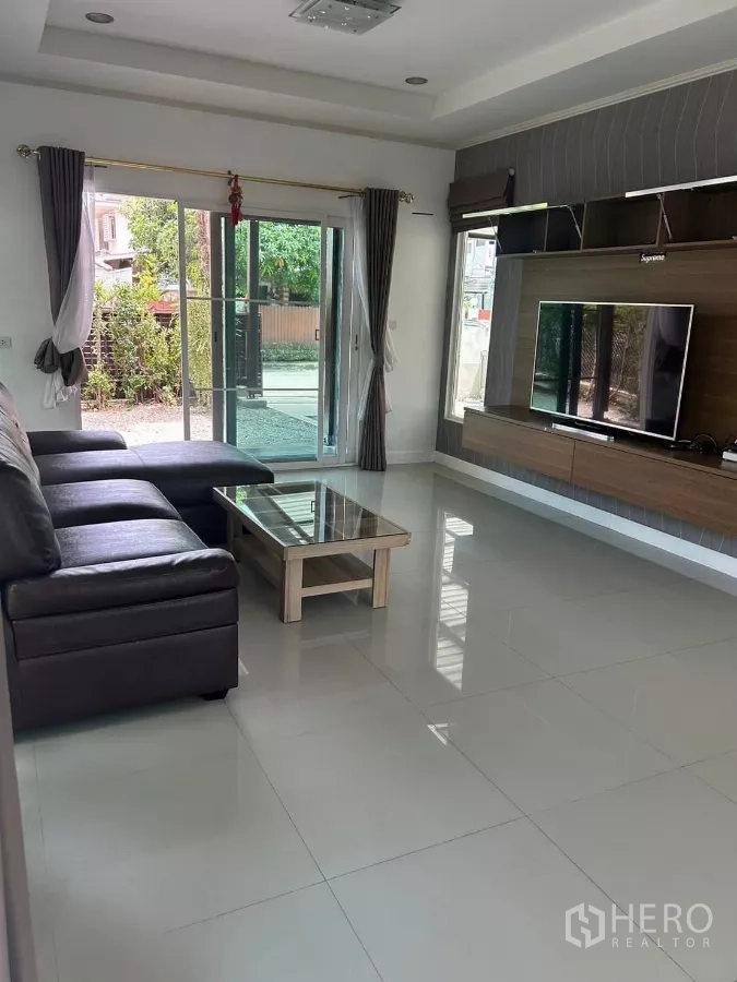 Detached House for rent or sale in Bang Phli, Samut Prakan - Bright living room with sectional sofa, built-in TV wall and glass doors to the garden.