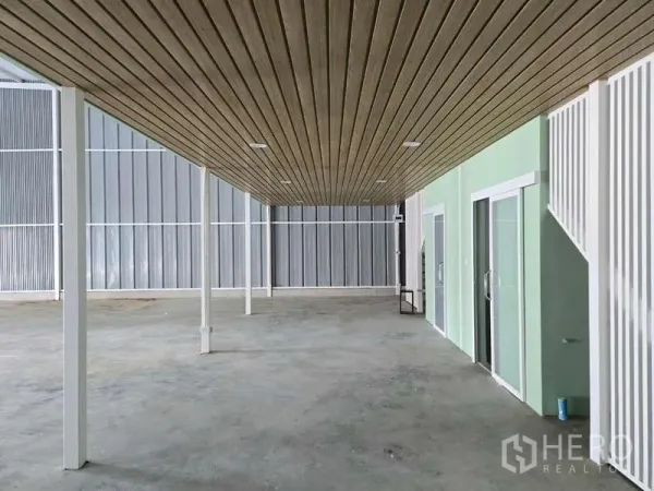 Warehouse for rent in Wang Thonglang, Bangkok - Open warehouse interior with high ceiling, concrete floor and glass-fronted rooms.
