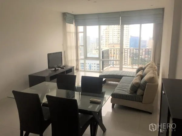 Condominium for rent or sale in Watthana, Bangkok - Bright living and dining area with glass table, sofa, TV console and floor-to-ceiling windows opening to a city-view balcony.