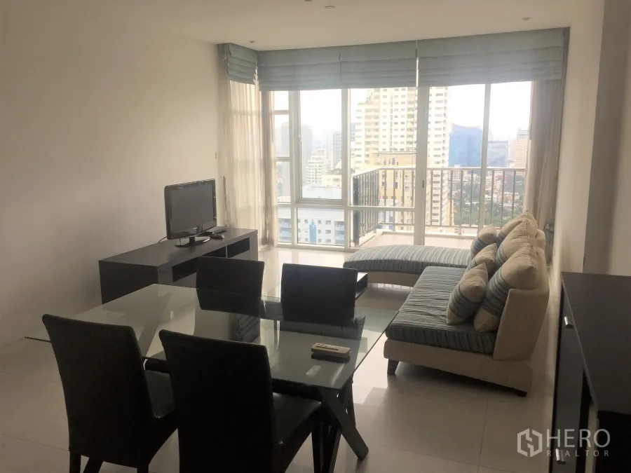 Condominium for rent or sale in Watthana, Bangkok - Bright living and dining area with glass table, sofa, TV console and floor-to-ceiling windows opening to a city-view balcony.