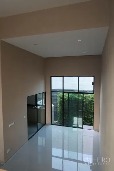 Townhouse for rent in Suan Luang, Bangkok - Double-height living area of a modern Suan Luang townhouse with floor-to-ceiling windows and glossy tile floors.
