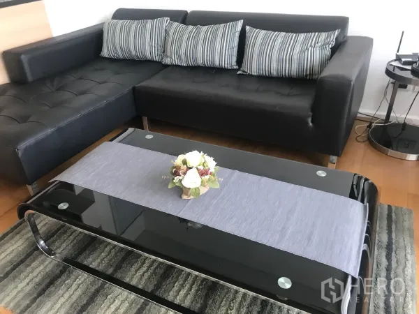 คอนโด ให้เช่าหรือขายในWatthana, Bangkok - มุมนั่งเล่น โซฟาหนังทรง L สีดำ กับโต๊ะกลางกระจกและพรม