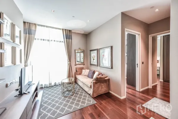 Condominium for rent or sale in Watthana, Bangkok - Open living space with TV console, large window, sofa and hallway leading to the bedrooms.