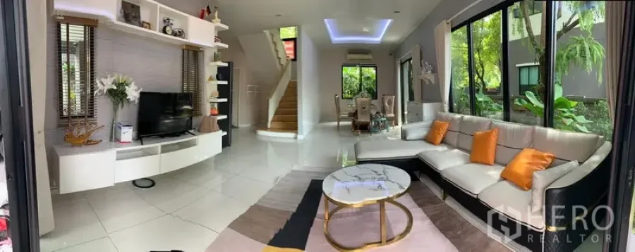 Detached House for rent in Bang Phli, Samut Prakan - Bright open-plan living room with L-shaped sofa, TV wall, marble coffee table, and large windows facing a green garden
