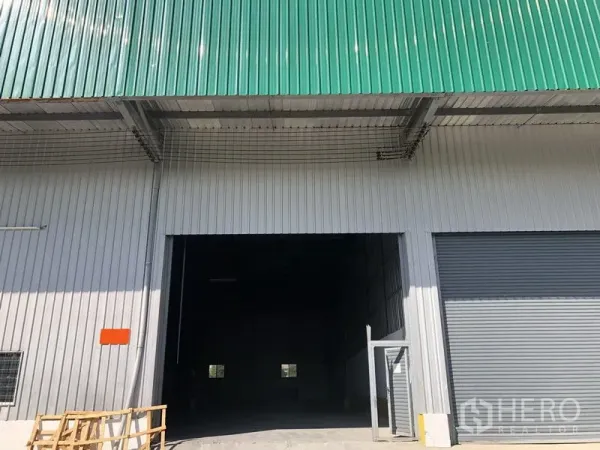 货栈 出租在Lat Krabang, Bangkok - 仓库外立面，绿色金属屋顶，大型卷闸门和宽敞装卸入口，位于曼谷Lat Krabang。