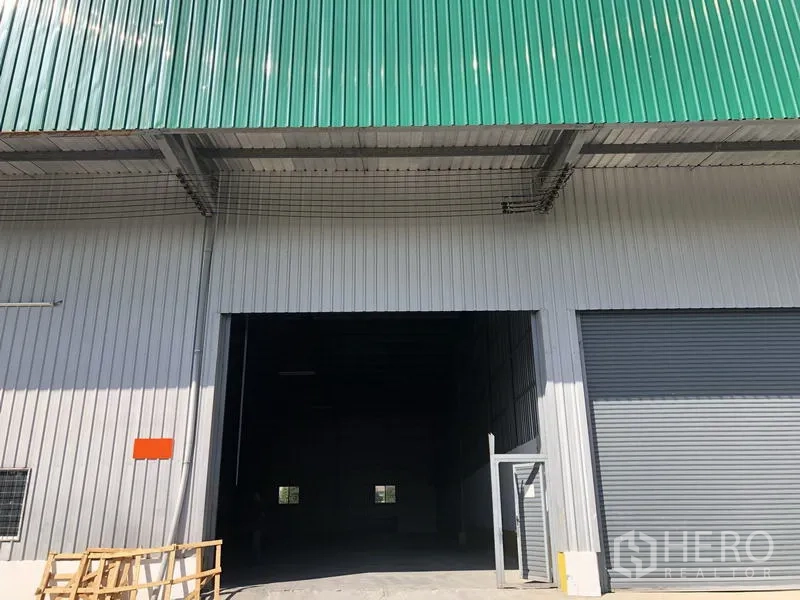货栈 出租在Lat Krabang, Bangkok - 仓库外立面，绿色金属屋顶，大型卷闸门和宽敞装卸入口，位于曼谷Lat Krabang。