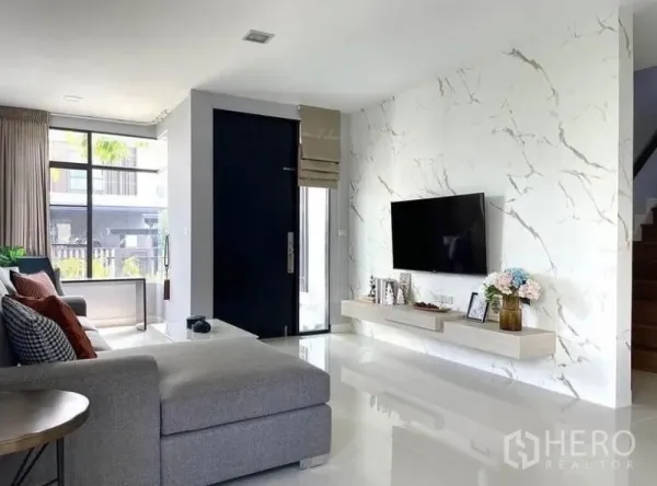 Detached House for rent in Prawet, Bangkok - Entrance lounge showing marble TV wall with floating shelf, large windows and staircase.