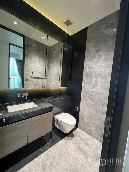 Condominium for rent - Contemporary bathroom with wall-hung toilet, large mirror, and marble wall tiles.