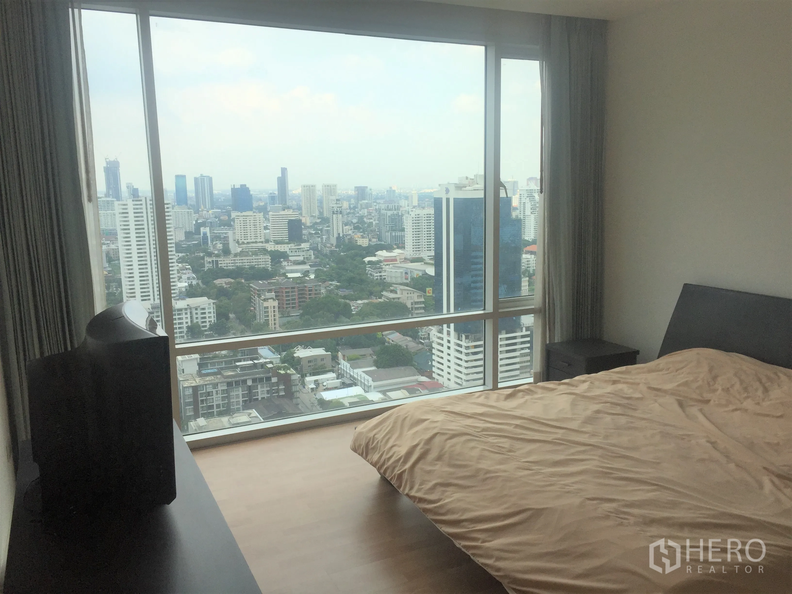 Condominium for rent or sale in Watthana, Bangkok - Master bedroom with a panoramic window framing wide city skyline views.
