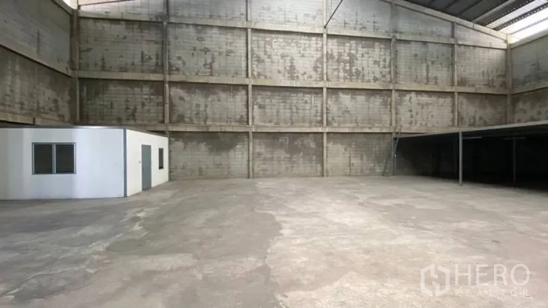 货栈 出租在Prawet, Bangkok - 高挑仓库全景，左侧为办公室盒体，右侧为夹层结构，地面为混凝土。