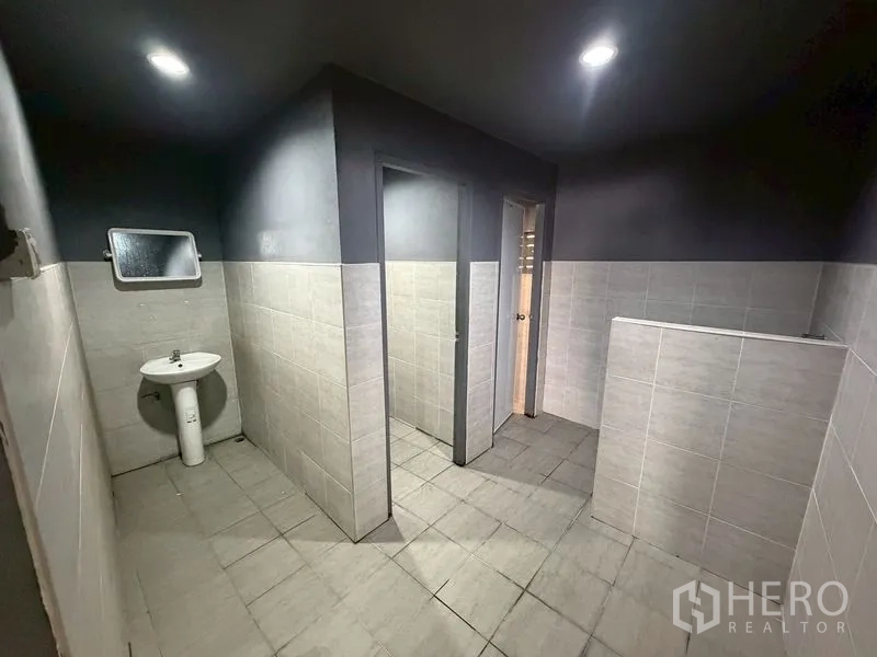 Warehouse for rent in Lat Phrao, Bangkok - Tiled restroom area with separate stalls and ceiling lights.