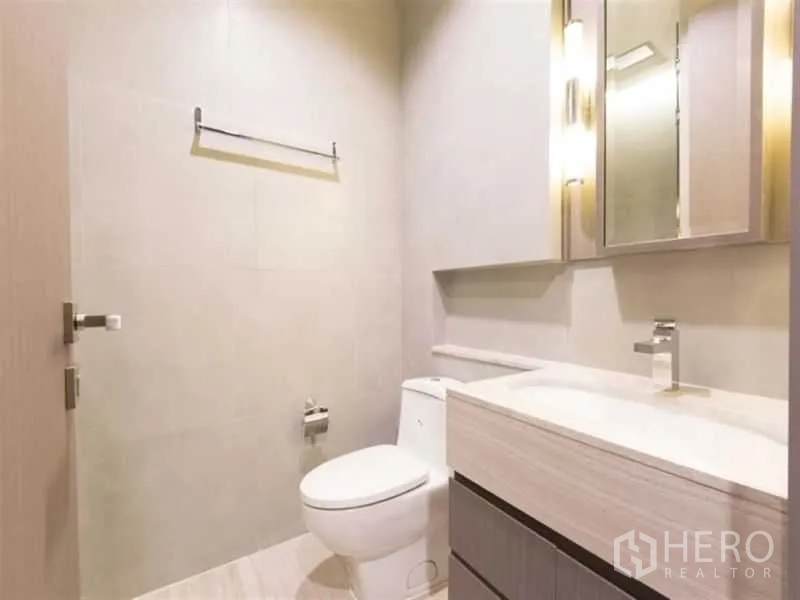 Condominium for rent in Bang Rak, Bangkok - Guest bathroom featuring a stone-top vanity, illuminated mirror and wall-hung fixtures.