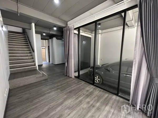 带办公室的家 出租或出售在Suan Luang, Bangkok - 底层空间设落地玻璃，可见有顶停车位与开放式楼梯。