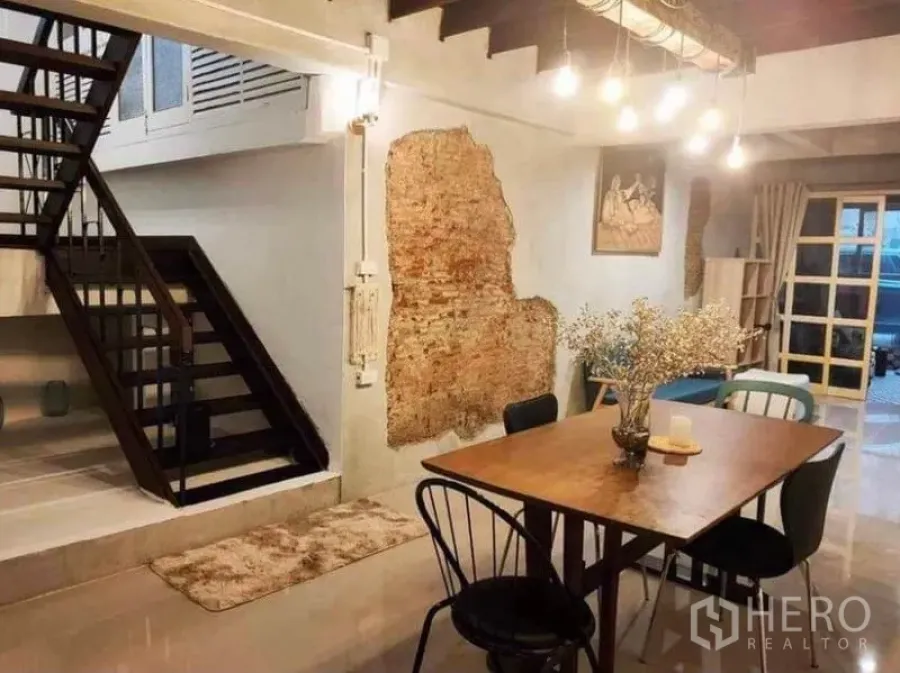 Detached House for rent in Pathum Wan, Bangkok - Dining area with wooden table, exposed brick feature wall and open staircase under pendant lights.