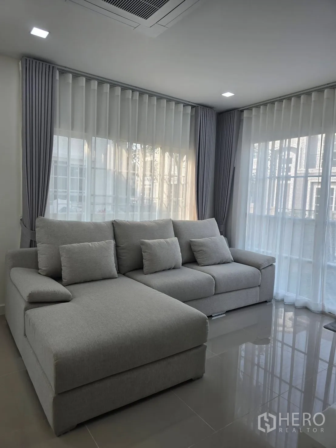 บ้านแฝด for rent in Mueang Samut Prakan, Samut Prakan - มุมนั่งเล่นมุมห้องพร้อมโซฟาแอลสีเทา ไฟฝังฝ้า และหน้าต่างกระจกมุมพร้อมผ้าม่าน
