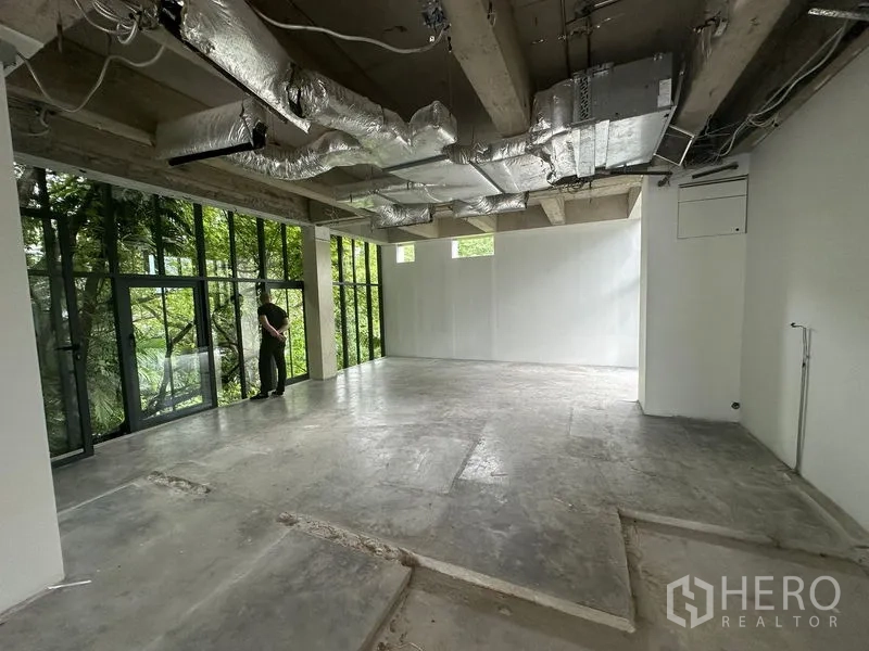 Office Space for rent in Khlong Toei, Bangkok - Corner office area with full-height glazing, concrete flooring and garden views through tall windows.