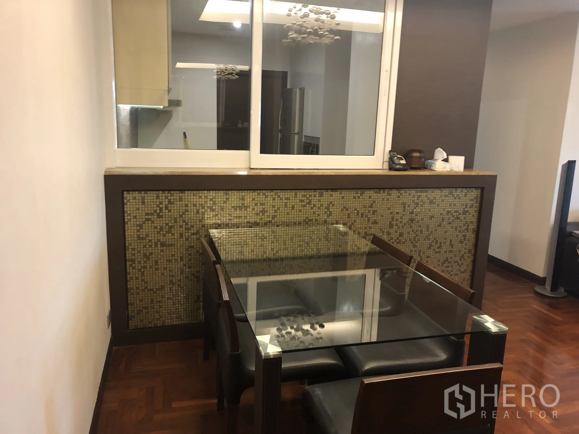 公寓 出租在Sathon, Bangkok - 餐区设玻璃餐桌与座椅，旁有传菜窗与马赛克特色墙。