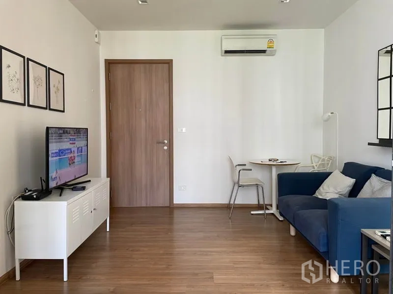 Condominium for sale in Watthana, Bangkok - Bright living room with wood flooring, TV console, round dining table, and a blue sofa.