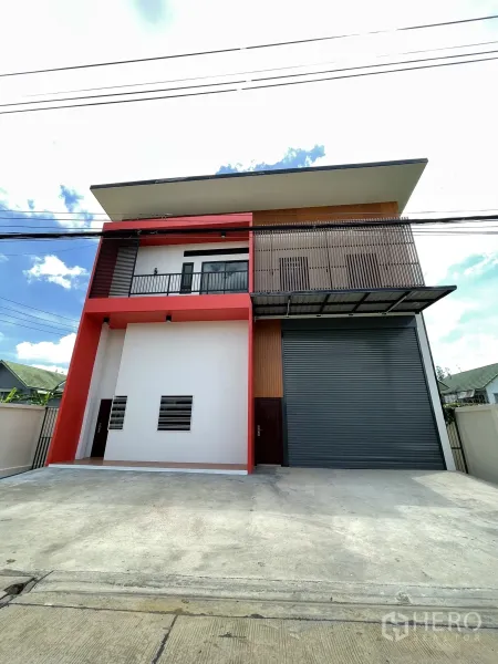 工厂 出租或出售在Lam Luk Ka, Pathum Thani - 两层迷你工厂外立面，红色框架、阳台与大型灰色卷闸门。