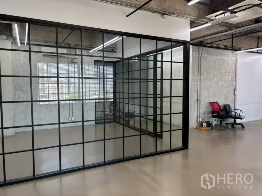 Office Space for rent in Watthana, Bangkok - Full-height black-framed glass meeting room beside windows with blinds in an industrial-style office.