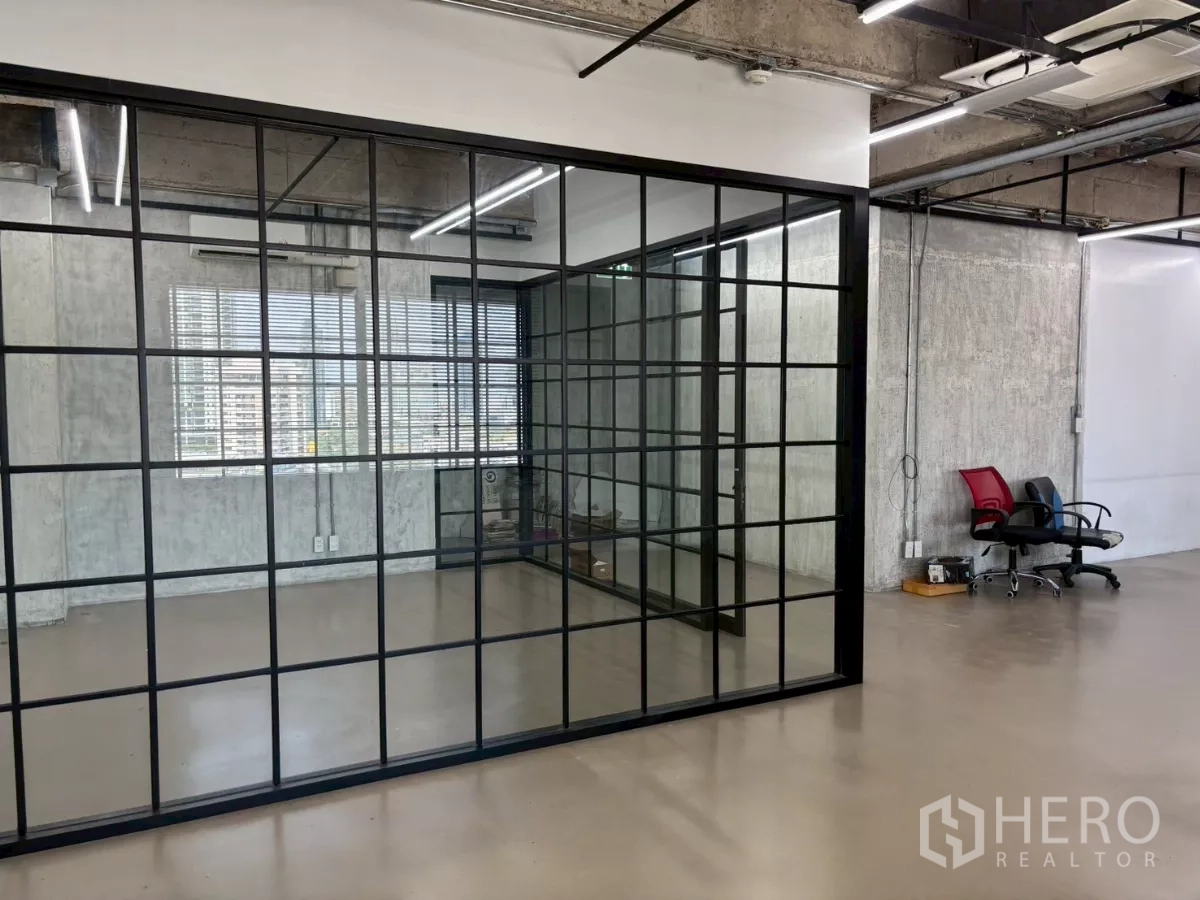 Office Space for rent in Watthana, Bangkok - Full-height black-framed glass meeting room beside windows with blinds in an industrial-style office.