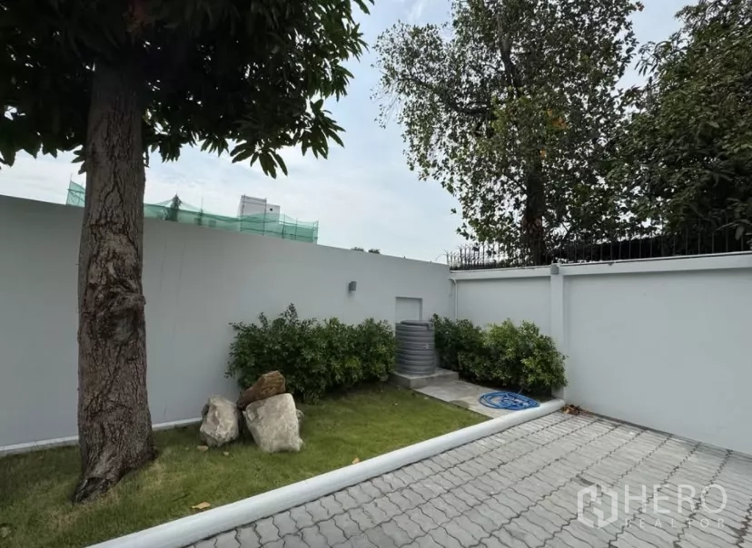 独立式住宅 出租在Watthana, Bangkok - 私家庭院一角，大树、灌木与铺装区。