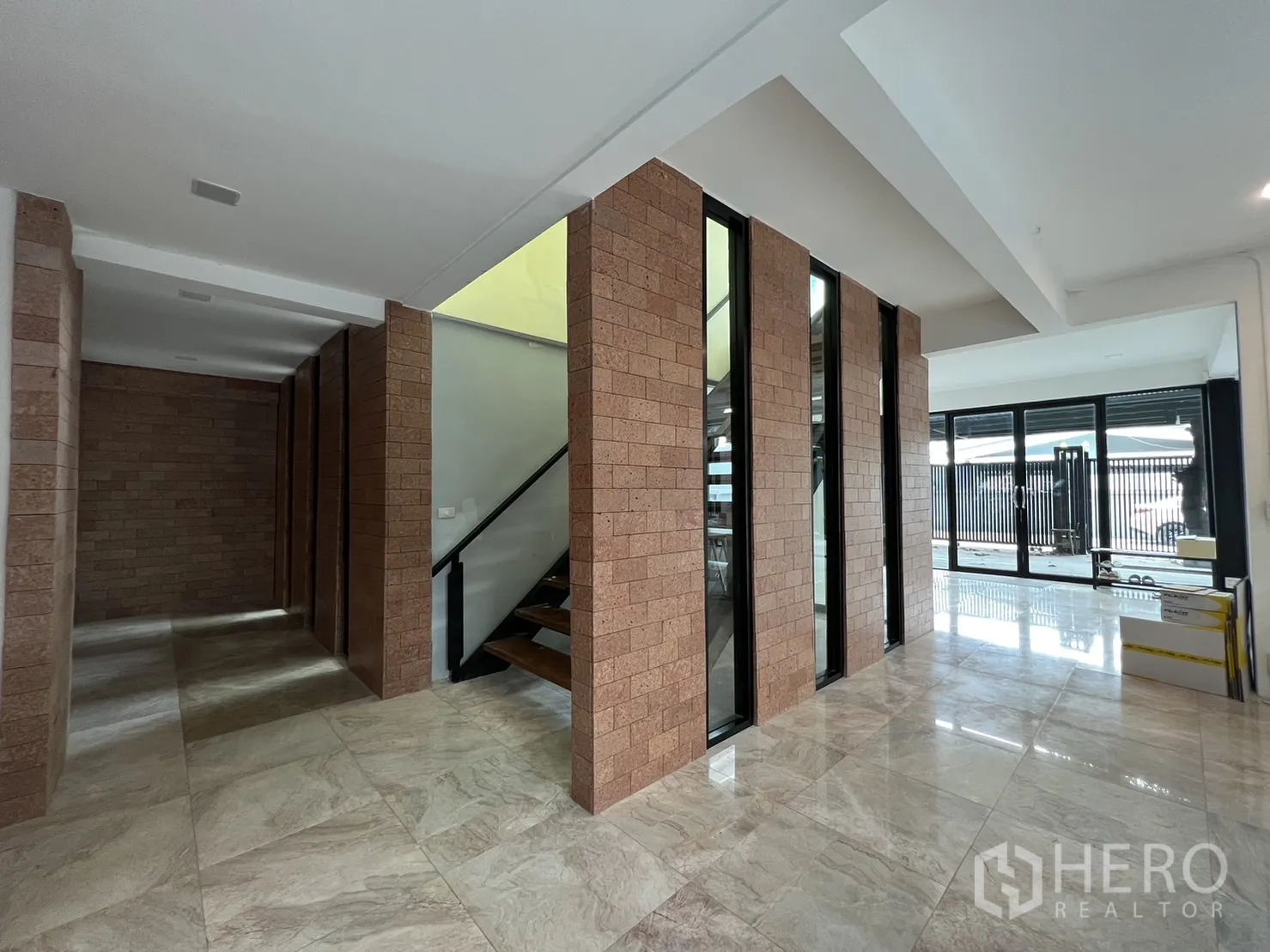 บ้าน ให้เช่าหรือขายในPhra Khanong, Bangkok - โถงชั้นล่าง เสากรุอิฐ พื้นกระเบื้องแผ่นใหญ่ และประตูกระจกสไลด์สู่ชาน