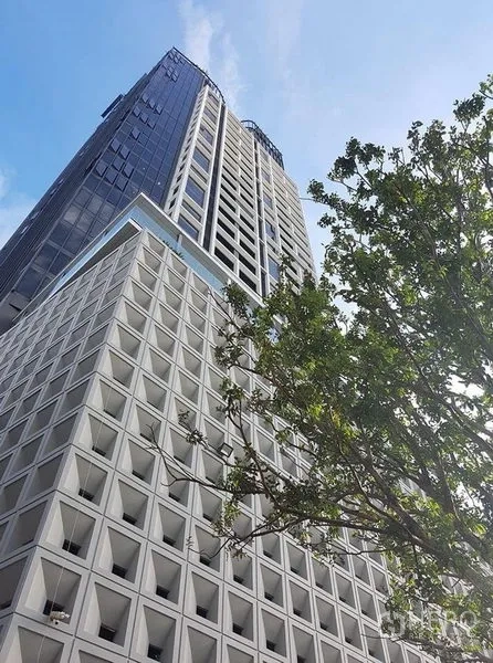 Condominium for rent in Khlong Toei, Bangkok - Modern high-rise condominium exterior with geometric facade and a tree in the foreground under blue sky.