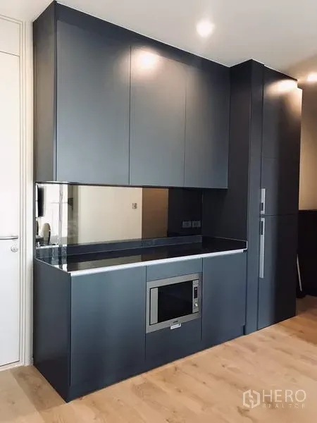 Condominium for rent or sale in Watthana, Bangkok - Sleek built‑in kitchen with dark cabinetry, mirrored backsplash, stone countertop, and integrated microwave.